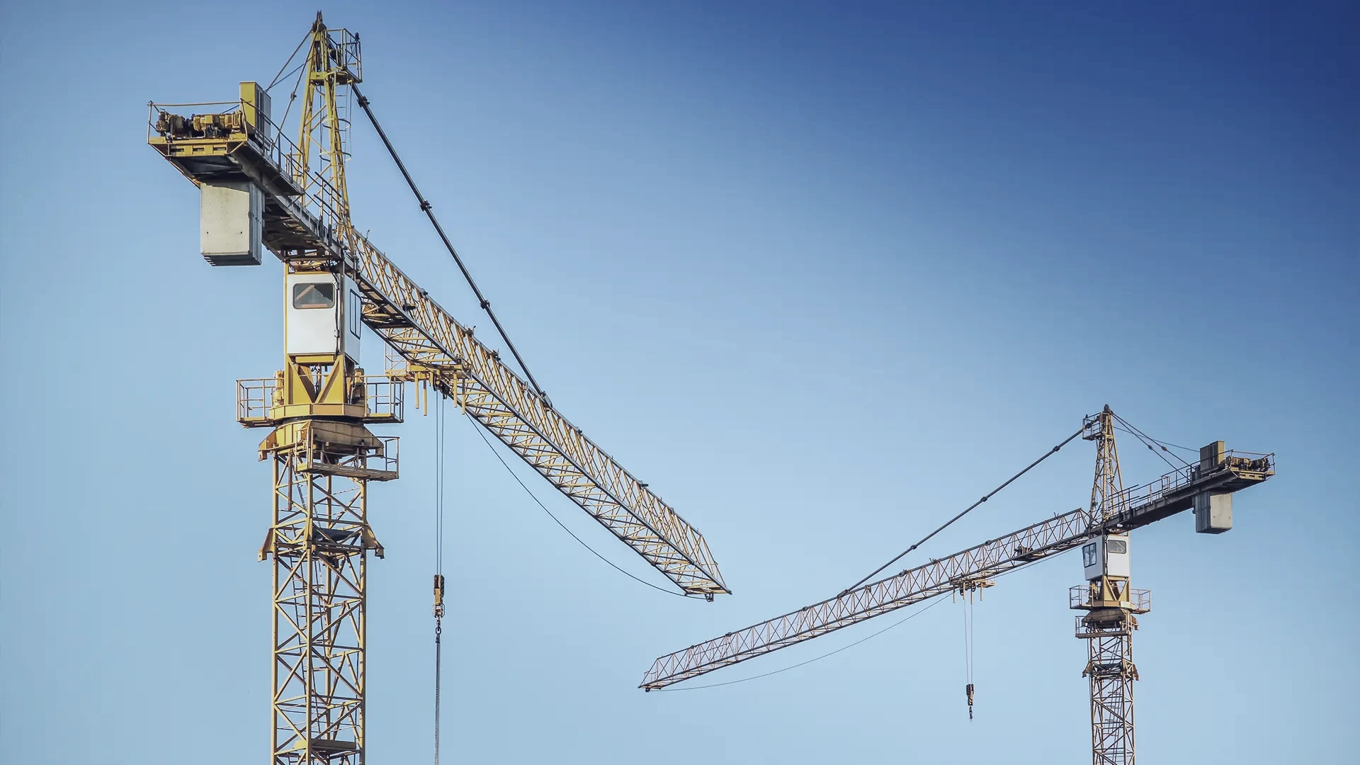 Two construction cranes against a blue sky
